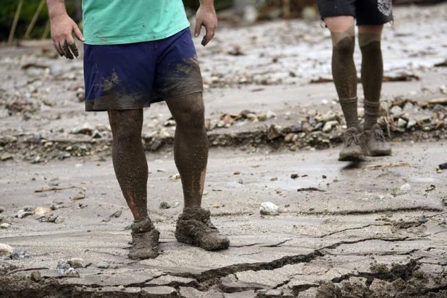 Residents Brooke Horspool, left, and his son Andrew Horspool show mud up to their knees while helping a neighbor in the aftermath of Tropical Storm Hilary Monday, Aug. 21, 2023, in Yucaipa, Calif. (AP Photo/Marcio Jose Sanchez)